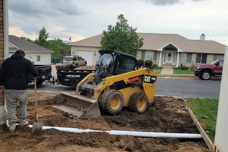 CAT skid steer, forms, drain pipe, and Morton & Sons trailer at a job site