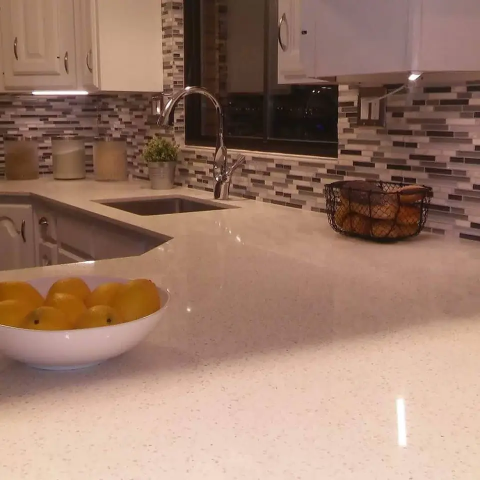 White kitchen countertops with an undermount sink and gray glass-tile backsplash