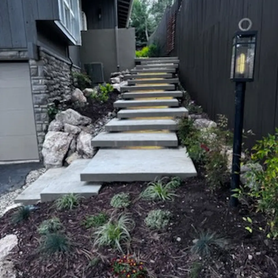 Floating concrete stairs with LED under-step lights beside a house, mulch and boulders