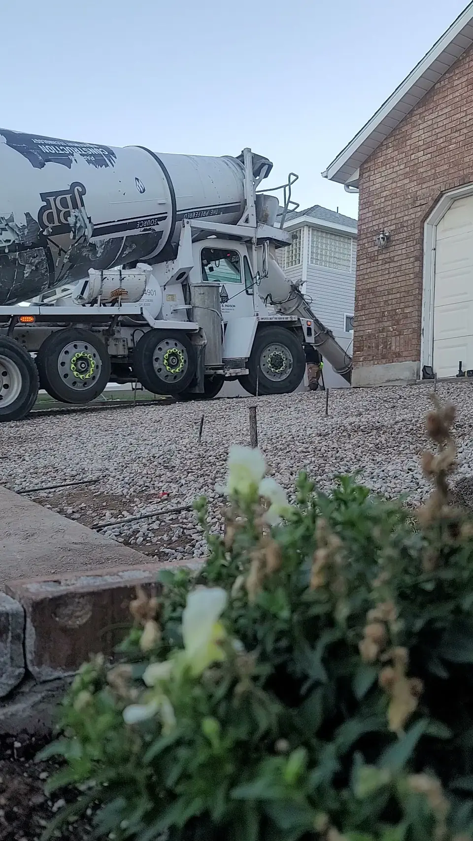 White mixer truck pouring concrete onto gravel beside a brick house