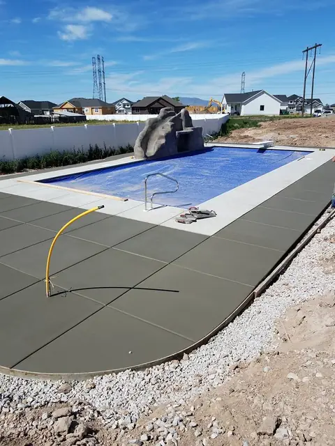 New concrete pool deck around a backyard swimming pool