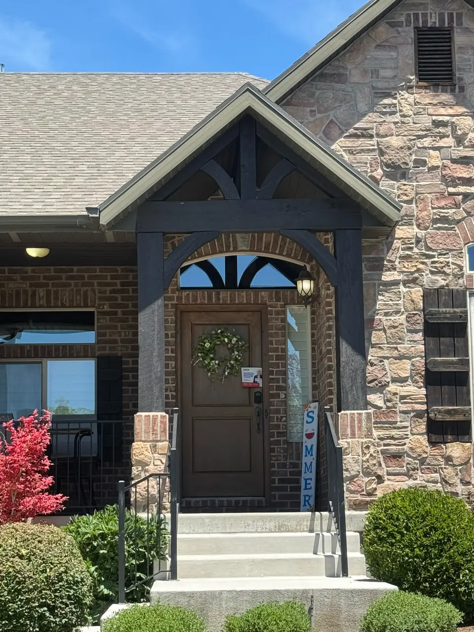 Restored dark-stained timber pillars and beams framing a home entry with brick and stone