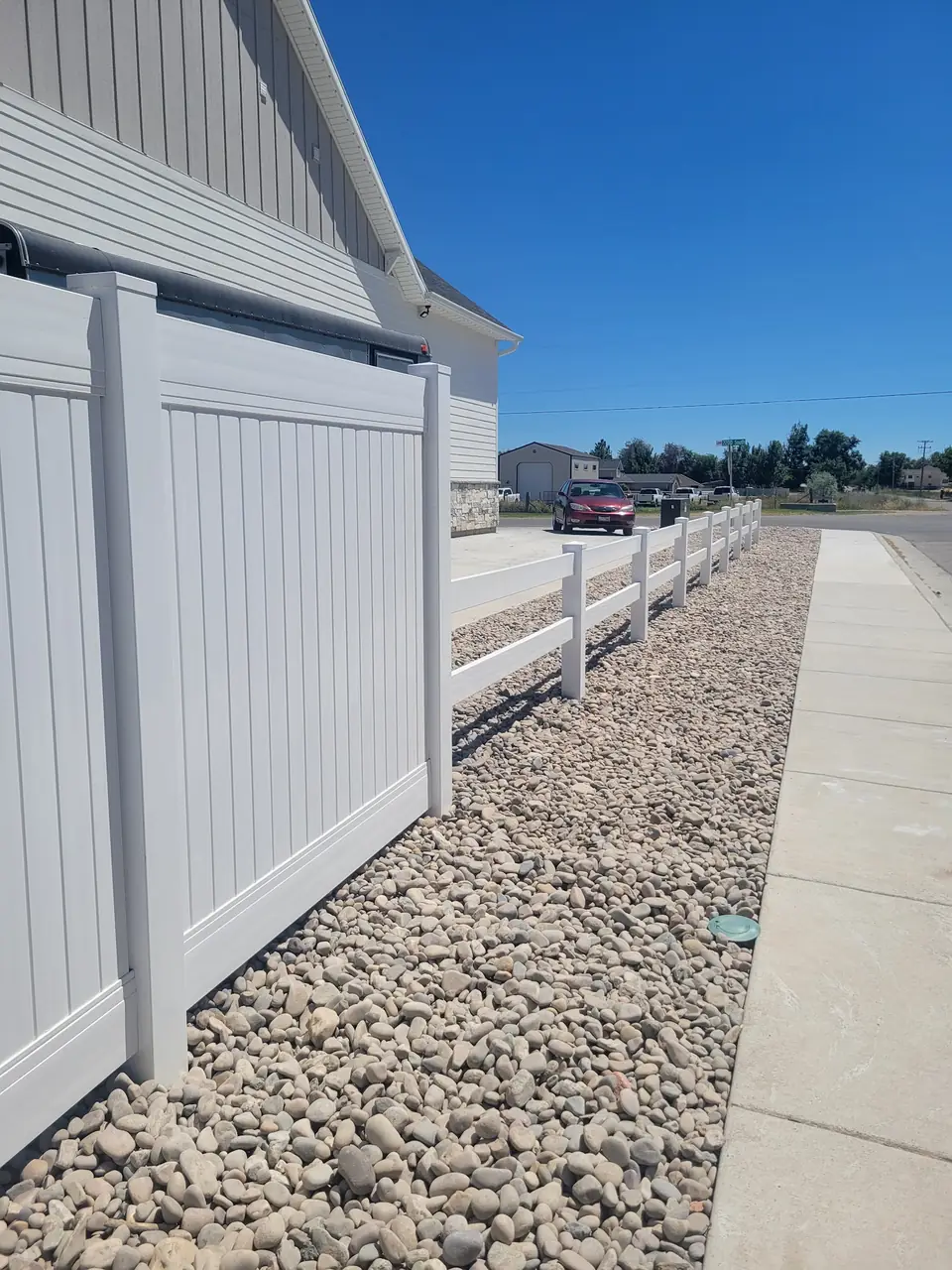 New white vinyl fence and three-rail fence beside a house